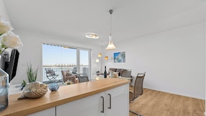 Una cocina moderna con encimera de madera, armarios blancos y un comedor con sillas de mimbre.