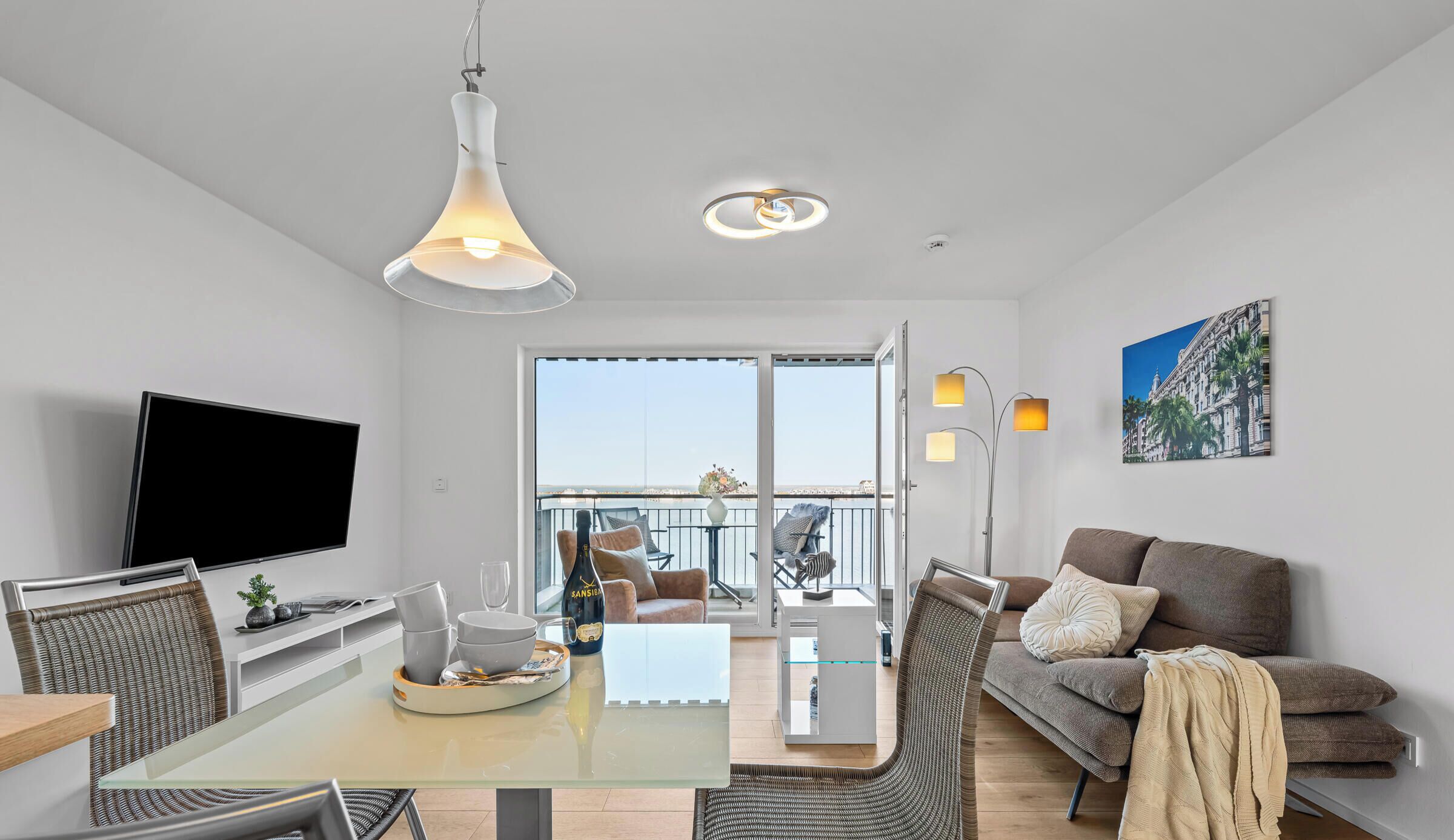 En moderne stue med et glasbord, en sofa, et fjernsyn og en balkon med udsigt.