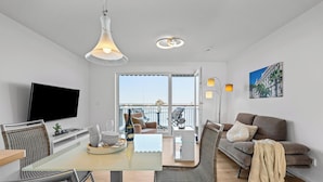 Una sala de estar moderna con una mesa de vidrio, un sofá, un televisor y un balcón con vistas.
