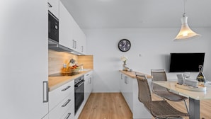 Una cocina moderna con encimera de madera, electrodomésticos de acero inoxidable y comedor con mesa de vidrio y sillas de mimbre.