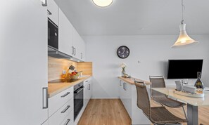 A modern kitchen with a wooden countertop, stainless steel appliances, and a dining area with a glass table and wicker chairs. - Cannes - 2nd Floor, Balcony, Harbor View, Private Parking, Washing Machine (Olpenitz)