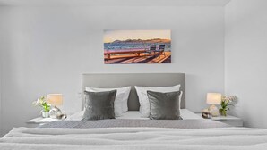 Un dormitorio con cama, dos mesitas de noche, dos lámparas, un cuadro y vistas al mar.