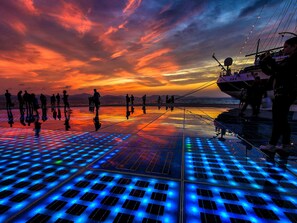 Ein Sonnenuntergang über einer spiegelnden Oberfläche, auf der Menschen entlanggehen, ein Boot fährt und eine Person ein Foto macht.