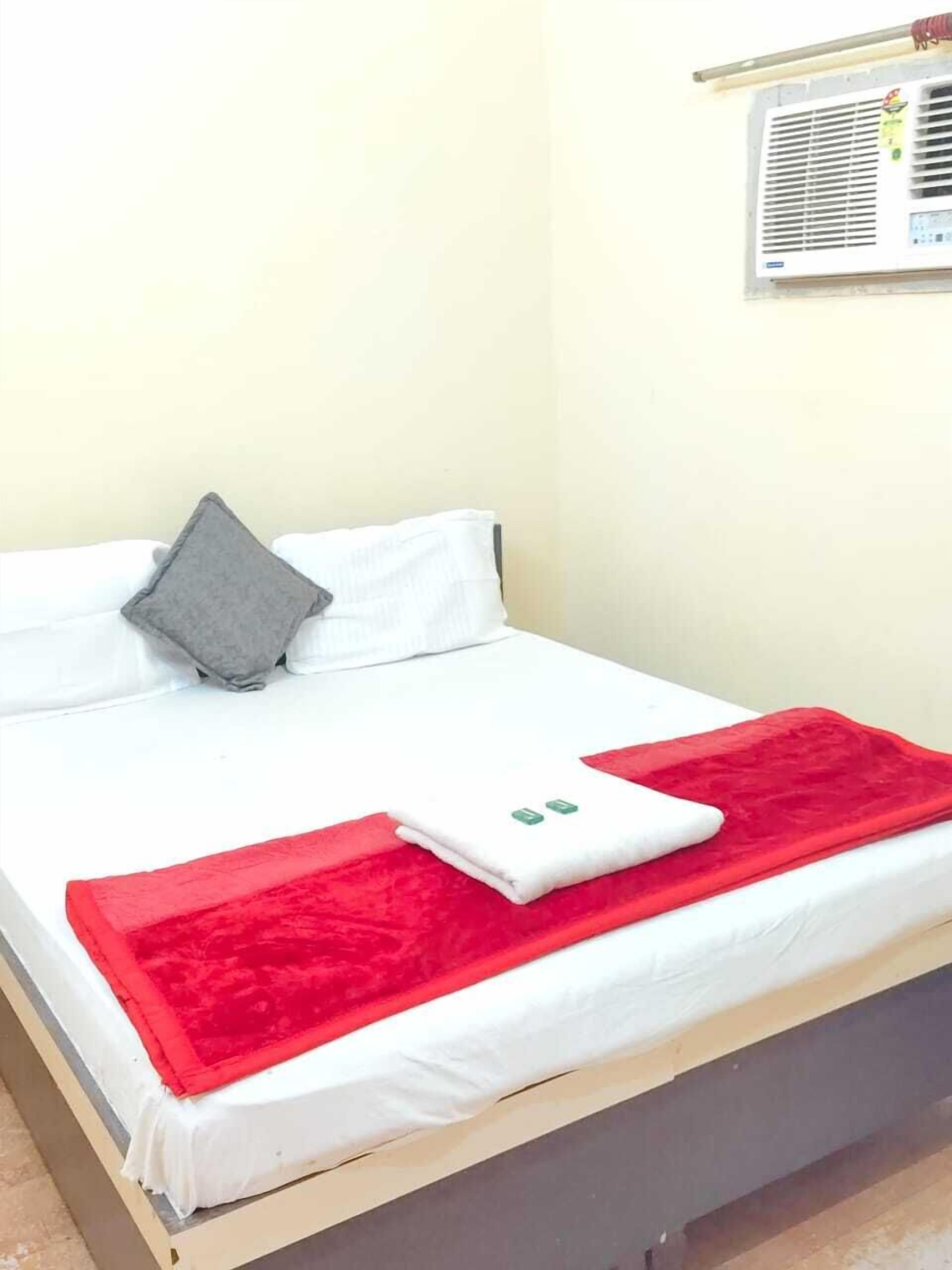 Una cama con ropa de cama blanca, una almohada gris y dos mantas rojas.
