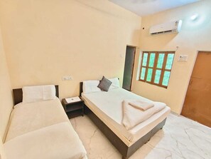 Une chambre d’hôtel avec deux lits simples, une table de chevet, un appareil de climatisation et une fenêtre donnant sur un paysage verdoyant.