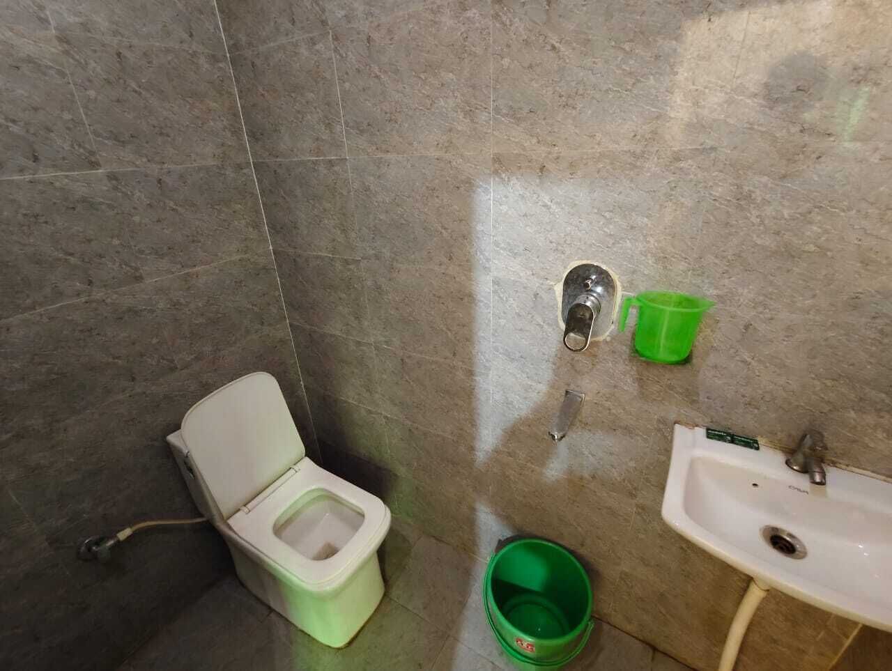A bathroom with a toilet, a sink, and a green bucket.