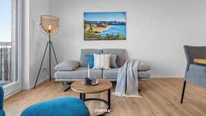 Una sala moderna con un sofá, una mesa de centro, una lámpara de pie y un cuadro de un paisaje costero.
