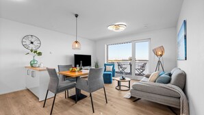 Un apartamento moderno con comedor, sala de estar con sofá, balcón con vistas y un reloj grande en la pared.