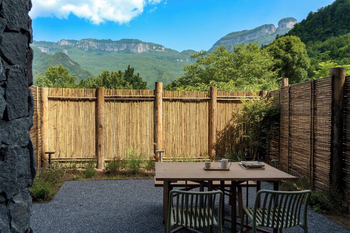 Eine Terrasse im Freien mit Tisch und Stühlen, einem Bambuszaun und Blick auf Berge.
