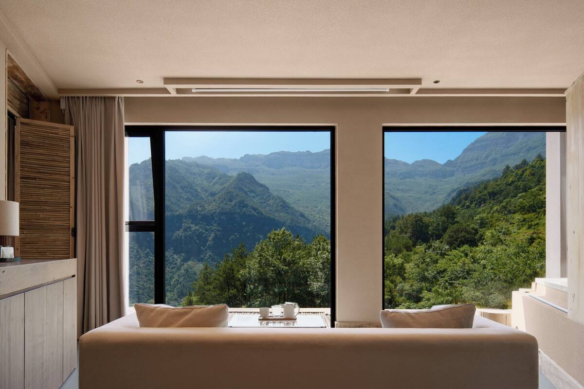 Ein Schlafzimmer mit einem großen Bett, zwei Fenstern mit Blick auf die Berge und einem hölzernen Kopfteil.