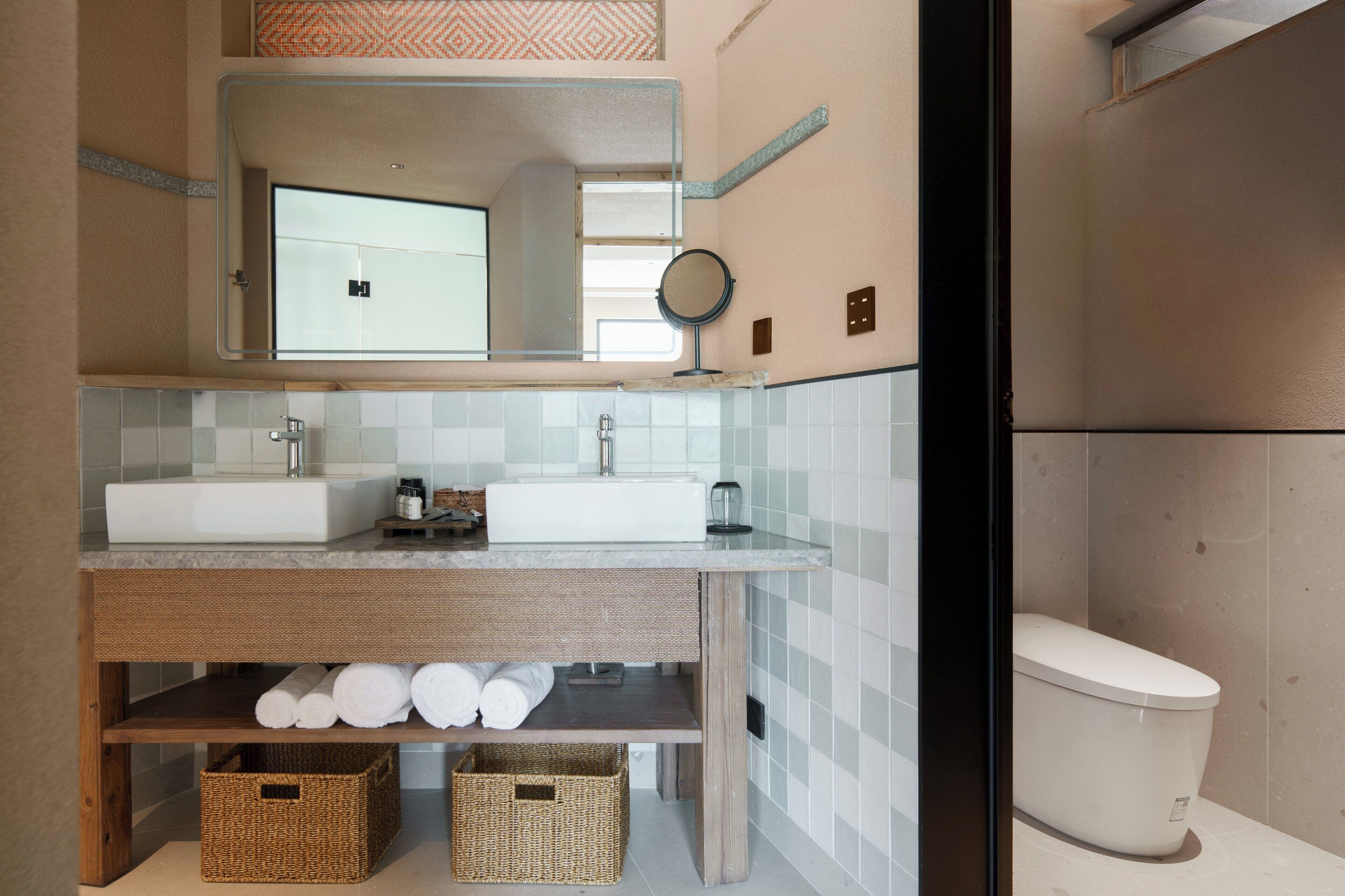 A bathroom with two sinks, a mirror, and a toilet. There are baskets under the sinks and a towel rack above them.
