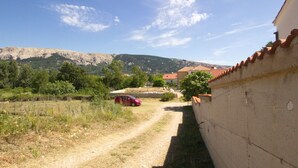 Una strada di campagna con un'auto rossa parcheggiata a lato, che conduce a un edificio con tetto in tegole rosse.