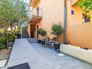 Ein Innenhof mit gefliestem Boden, Außenbestuhlung, Topfpflanzen und einer Treppe, die zu einer Wohnung führt.