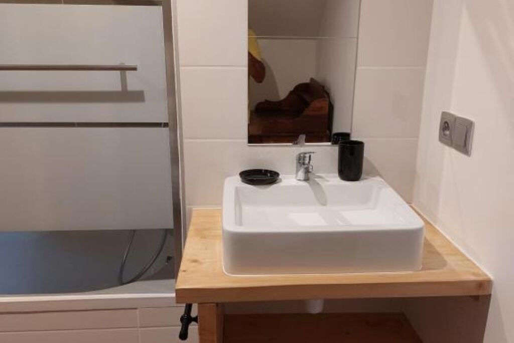 Une salle de bain avec un lavabo blanc, un plan de toilette en bois et un miroir.