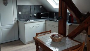 Une cuisine compacte avec des meubles blancs, un four à micro-ondes et une table à manger agrémentée d’un panier.