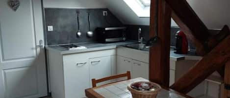 Une cuisine compacte avec des meubles blancs, un four à micro-ondes et une table à manger agrémentée d’un panier.