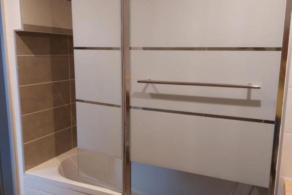 A bathroom with a glass-enclosed shower, white tiled walls, and a metal towel rack.