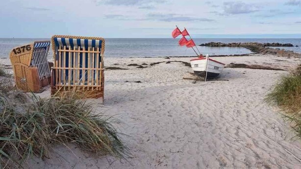 Una playa con una fila de sillas y un pequeño bote con una bandera roja.