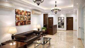 A modern lobby with a leather sofa, a glass coffee table, and a reception desk. - EMBLEM Hotel – Arjun Marg, Golf Course Road Gurgaon (Gurugram)