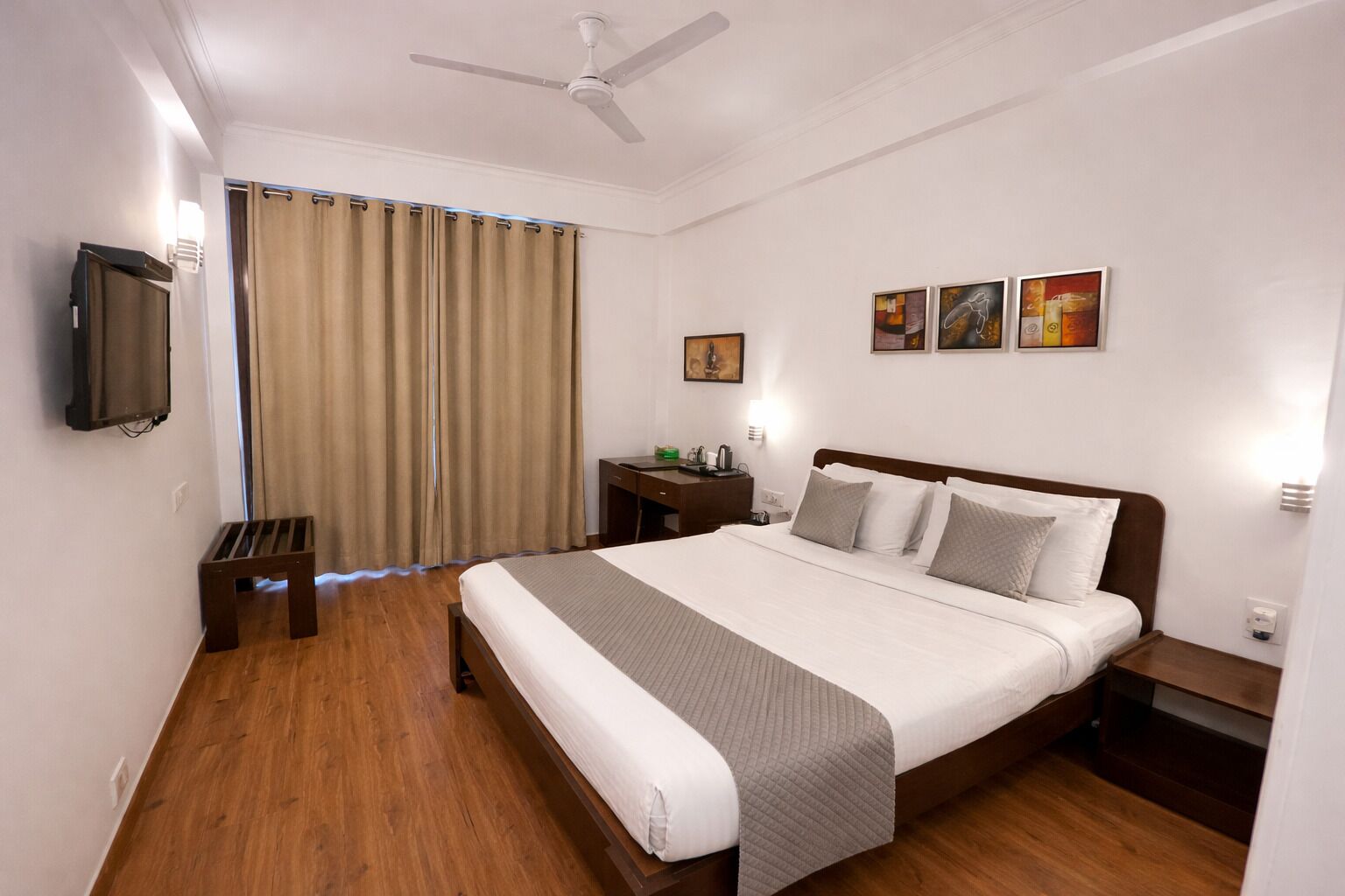 A hotel room with a bed, a desk, a chair, a television, and a ceiling fan.