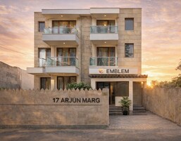 Un edificio moderno de varios pisos con un letrero que dice “EMBLEM” y una placa que indica “17 ARJUN MARG”.