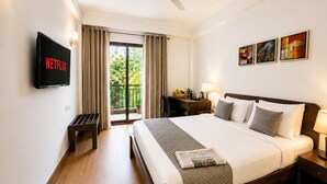 A hotel room with a bed, a desk, a chair, a TV, a balcony with curtains, and artwork on the wall. - EMBLEM Hotel – Arjun Marg, Golf Course Road Gurgaon (Gurugram)