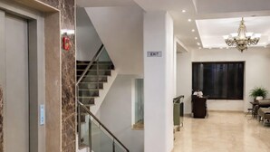 A hotel lobby with a marble floor, a staircase, a reception desk, and a chandelier. - EMBLEM Hotel – Arjun Marg, Golf Course Road Gurgaon (Gurugram)