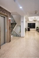 Un vestíbulo de hotel con suelo de mármol, una escalera, un mostrador de recepción y una araña.