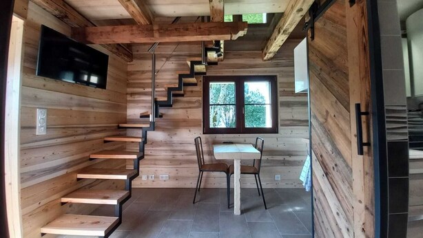 Ein Holzinnenraum mit Treppe, Essbereich und an der Wand befestigtem Fernseher.