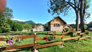 Ein rustikaler Holzzaun mit Blumenkästen, ein Steinhaus mit Strohdach und eine Bergkulisse im Hintergrund.