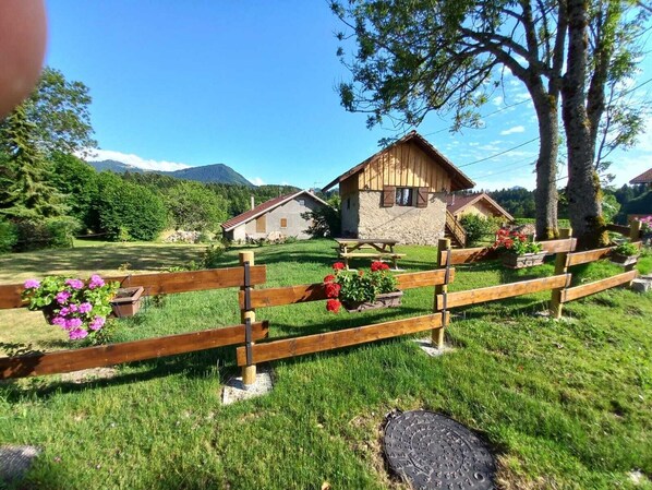 A rustic wooden fence with flower boxes, a stone house with a thatched roof, and a mountain backdrop.