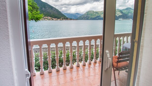 Een balkon met een witte balustrade met uitzicht op een meer, met bergen op de achtergrond.