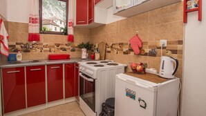 Een kleine keuken met rode kastjes, een witte kookplaat en een kleine koelkast.