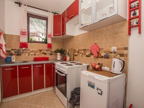 A compact kitchen with red cabinets, a white stove, and a small refrigerator. - Ferienappartement am Meer mit Terrasse by Interhome (Bigova)