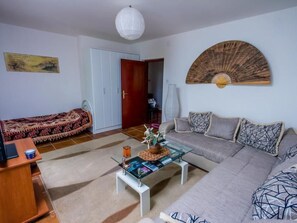 A living room with a sofa, a glass coffee table, a bed with a patterned blanket, a wooden cabinet, and a wall-mounted fan. - Ferienappartement am Meer mit Terrasse by Interhome (Bigova)