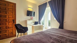 Un dormitorio con una cama grande, un escritorio con una computadora portátil, una silla y un televisor en la pared.