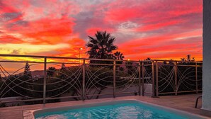 Una piscina con vista al atardecer, rodeada por una cerca metálica y palmeras.