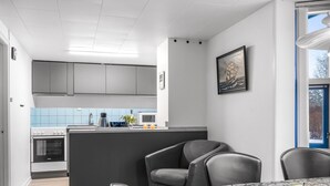 Eine moderne Küche mit grauen Schränken, einer Mikrowelle und einem Spülbecken. Es gibt einen Essbereich mit einem runden Tisch und Stühlen, sowie ein Fenster mit Blick auf Bäume.