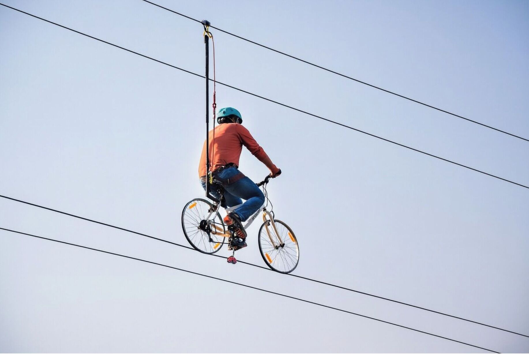 Eine Person zeigt eine Drahtseilkunst auf einem Fahrrad zwischen Stromleitungen.