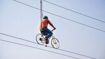 Eine Person zeigt eine Drahtseilkunst auf einem Fahrrad zwischen Stromleitungen.