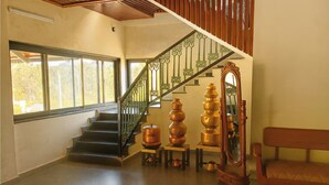 A staircase with ornate railings, a wooden bench, and a series of copper pots on the floor. - Sonemale Resort Chikmagalur (Mudigere)
