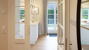 Un pasillo que da a una cocina con vistas al exterior, una ventana con cortinas y una lámpara colgante.