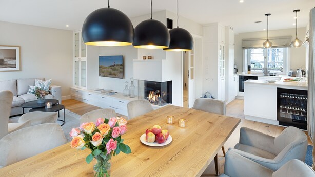 Una cocina moderna con una isla central, iluminación colgante y un comedor con mesa y sillas de madera.