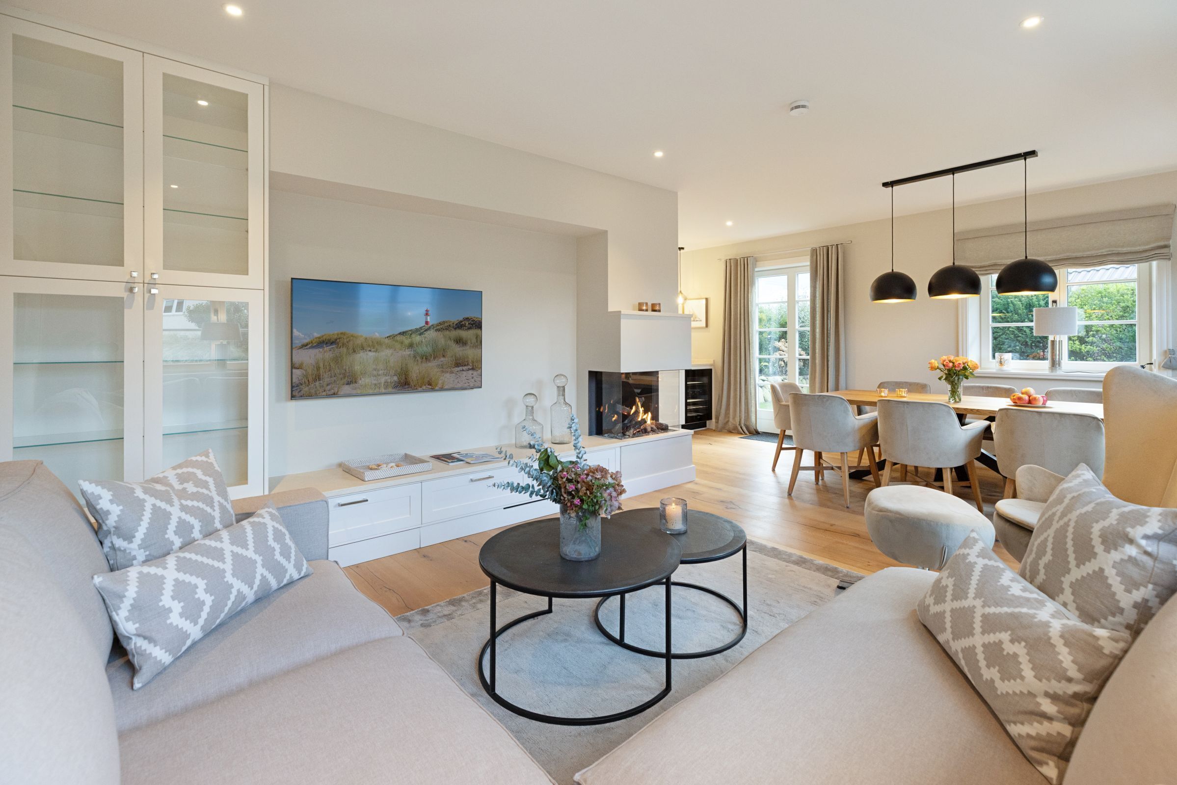 A modern living room with a sofa, coffee table, and a fireplace. There is a dining area with chairs and a table.
