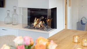 Una sala de estar moderna con una chimenea de vidrio, una mesa de madera con velas y un florero con flores.