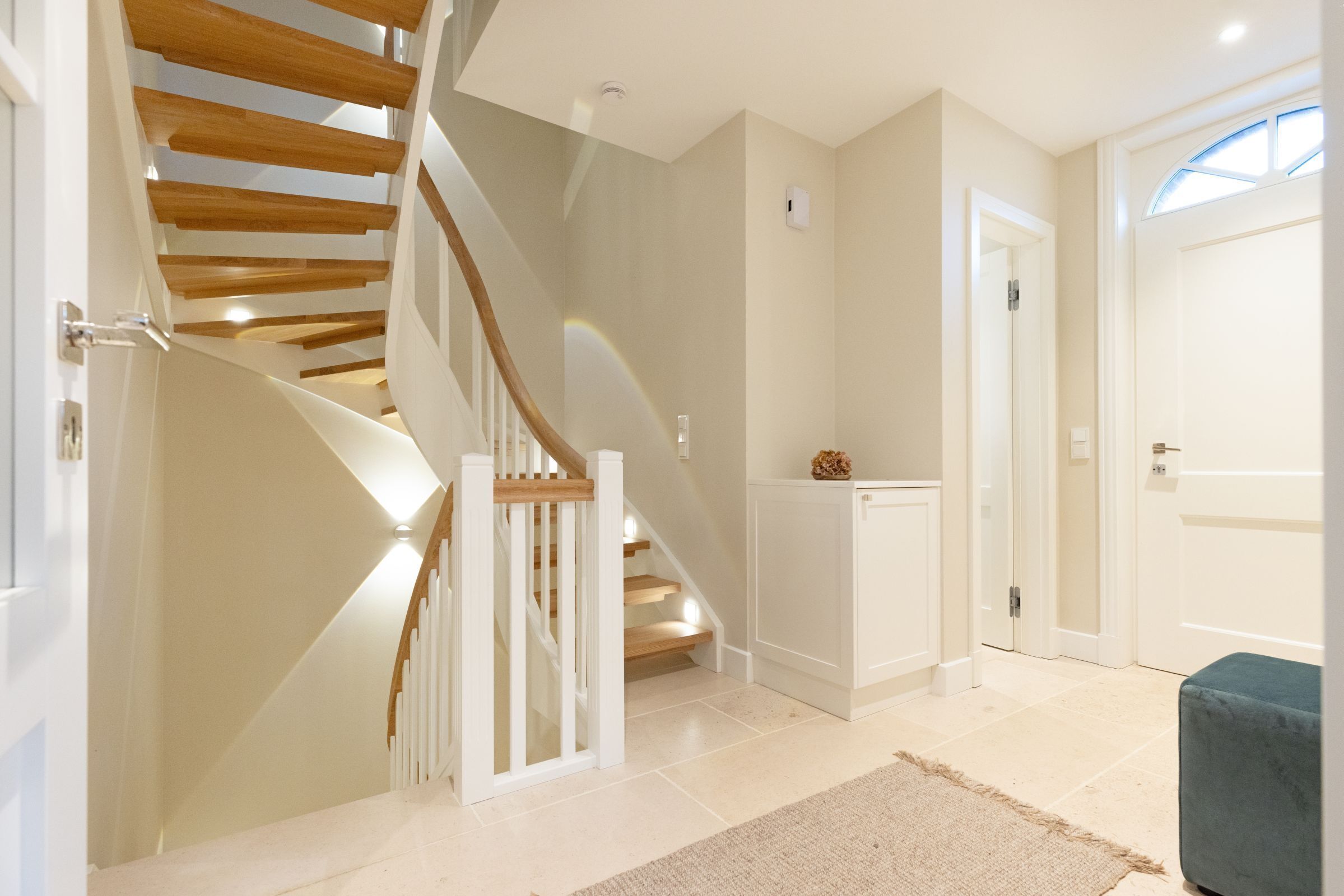 A modern interior with a curved staircase, a small cabinet, and a door leading to another room.