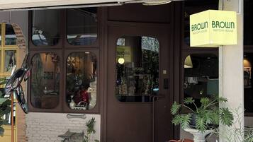 Fachada con una puerta marrón, un letrero que dice 'BROWN MATCHA HOUSE' y una bicicleta estacionada afuera.