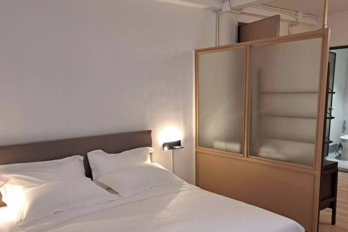 A modern hotel room with a large bed, a wooden headboard, and a nightstand with a lamp.