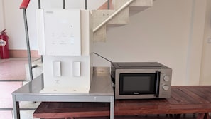 A kitchen area with a microwave and a water dispenser on a metal table. - Brown H (Bangkok)