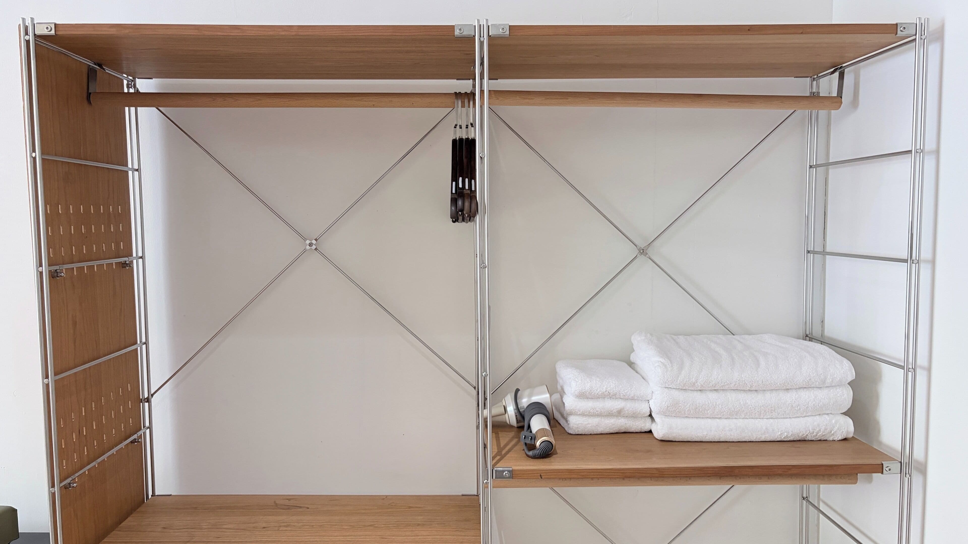 A room with a wooden wardrobe, a metal shelf with towels, and a camera on the shelf.